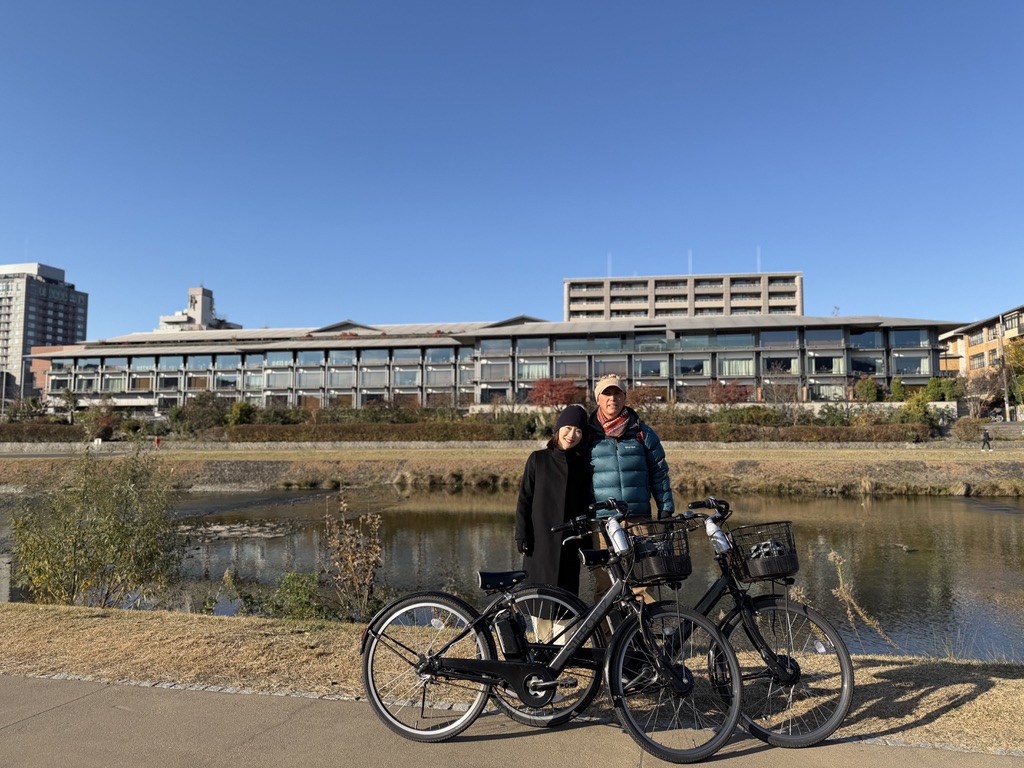 鴨川沿いで電動自転車と共に記念撮影する夫婦。